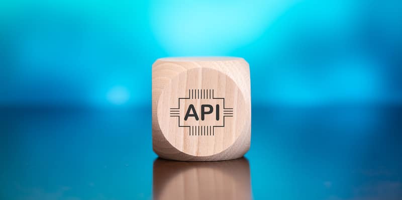 A wooden cube with the letters API on its side is centered in the image, symbolizing innovation in white label software. The background features a gradient of blue shades, creating a soft, blurred effect.
