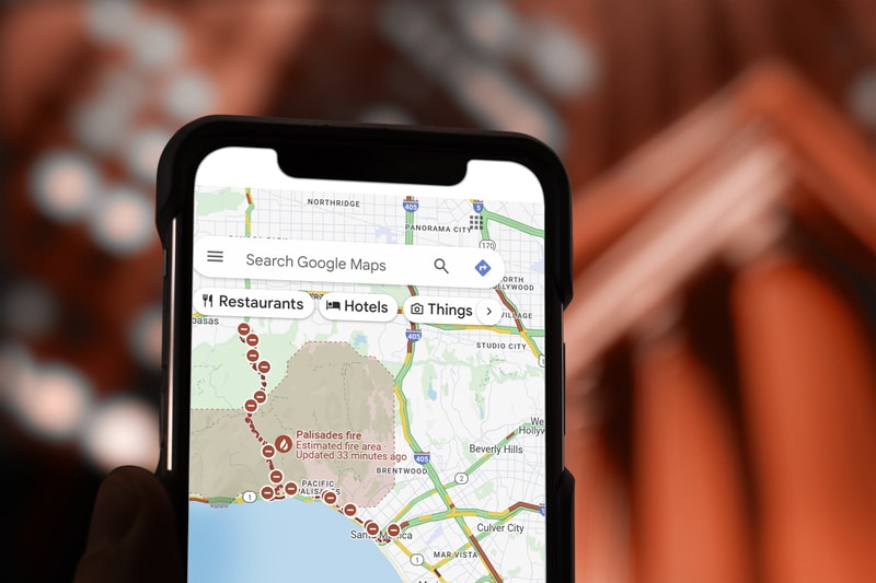 A smartphone displays Google Maps showing a fire-affected area near Pacific Palisades, California, enhancing local search visibility with marked locations and options for restaurants, hotels, and things to do.